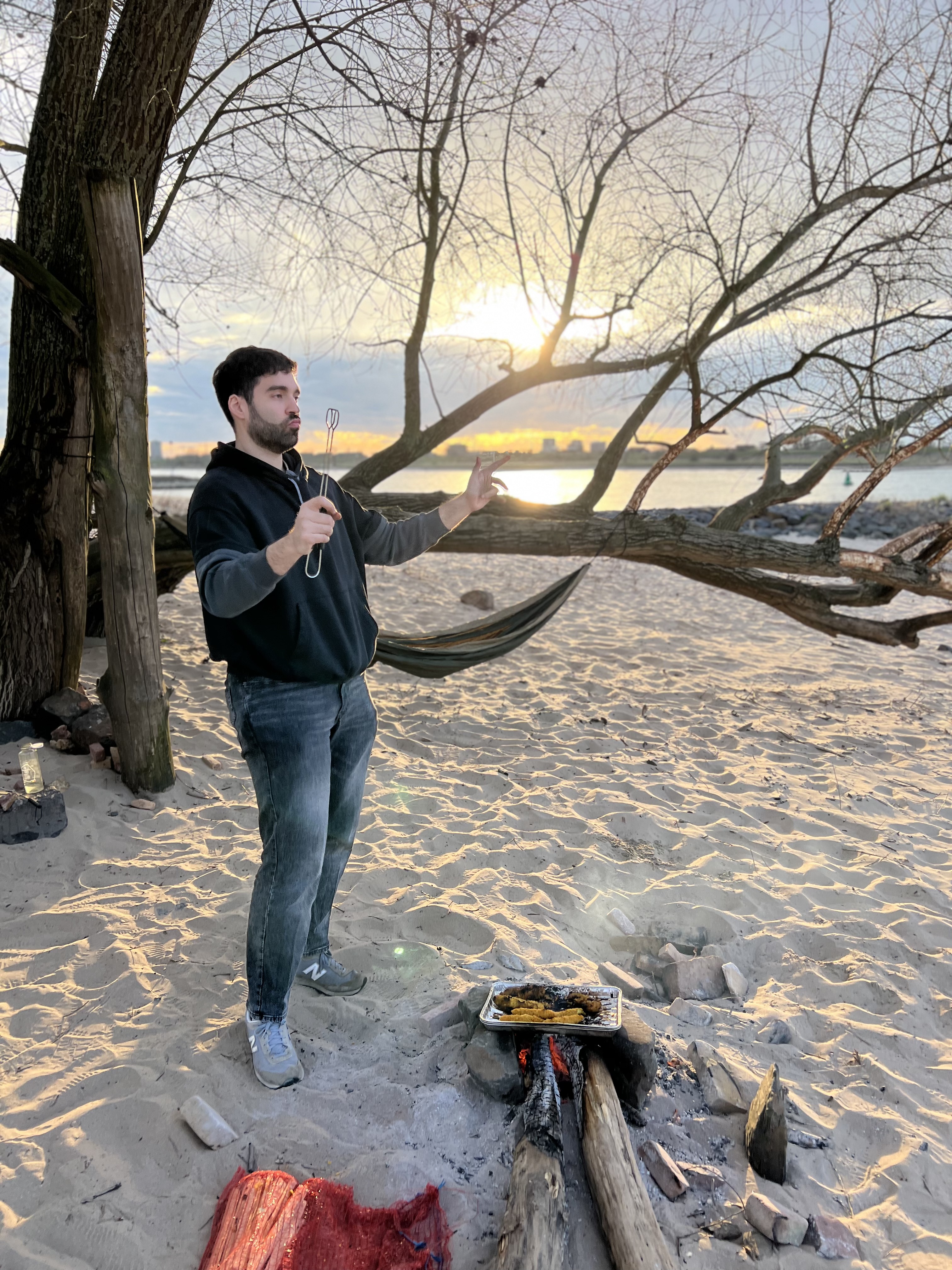 A cook tending a small driftwood fire at sunset on a sandy shore.