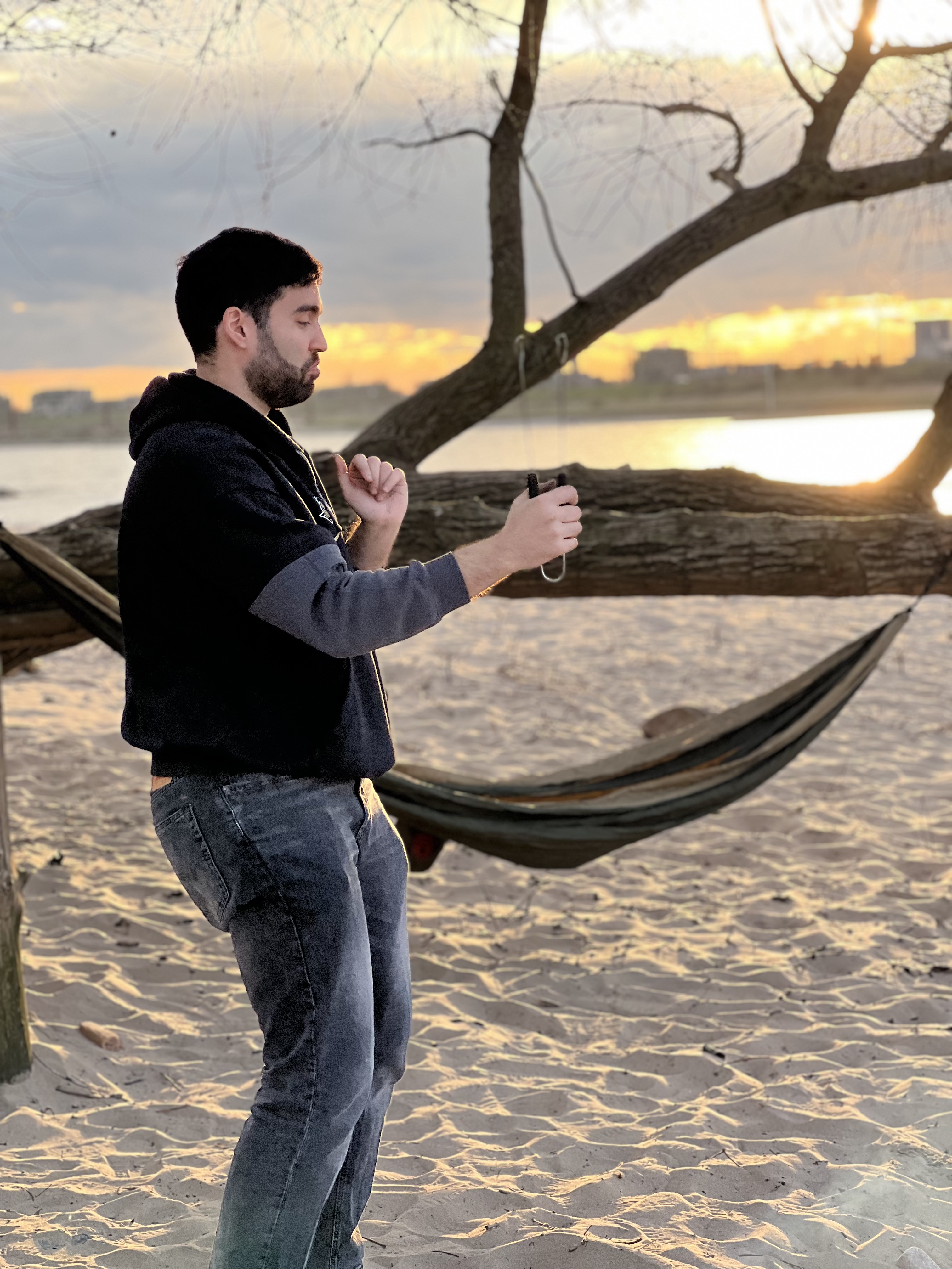 A person standing by a hammock at sunset, river behind, lost in a moment.