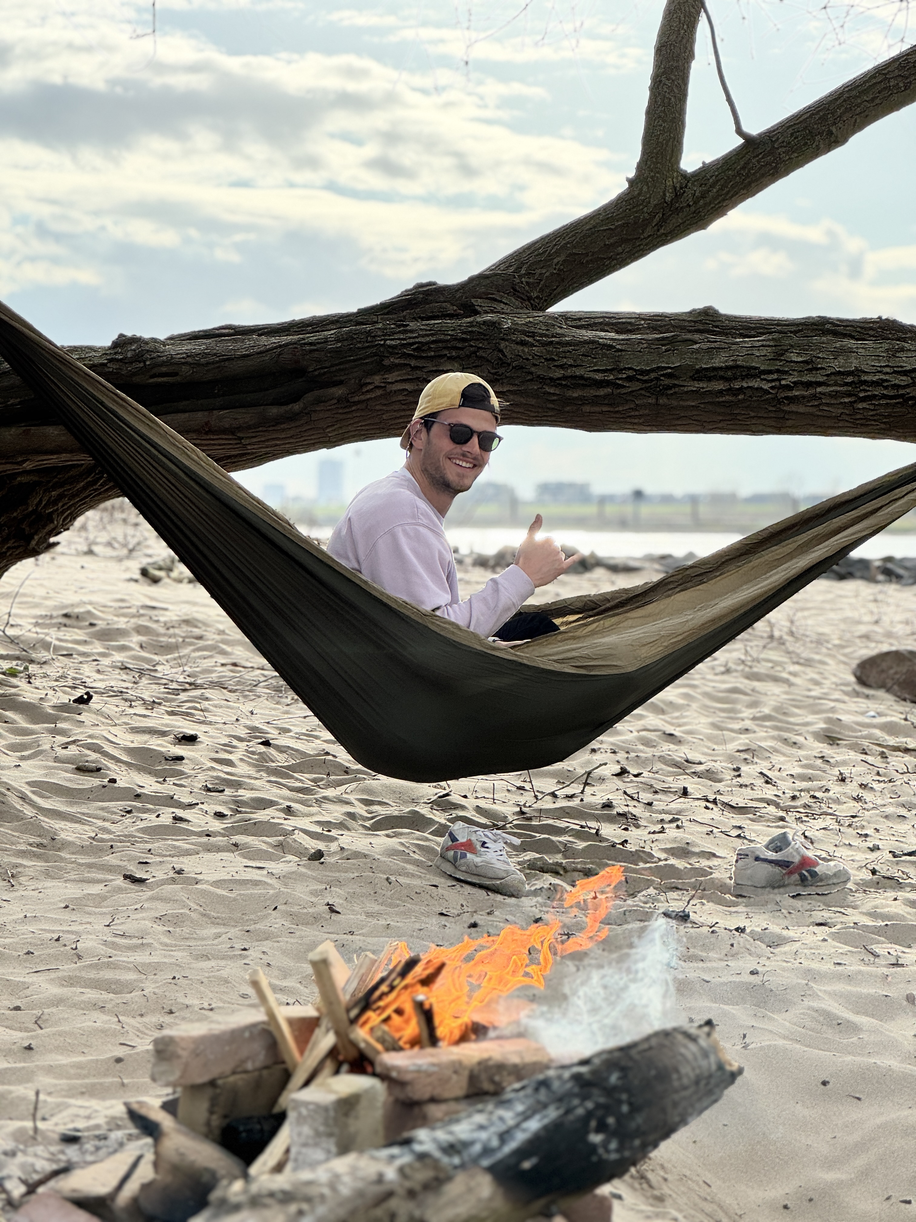 A friend in a hammock between trees, small campfire nearby.